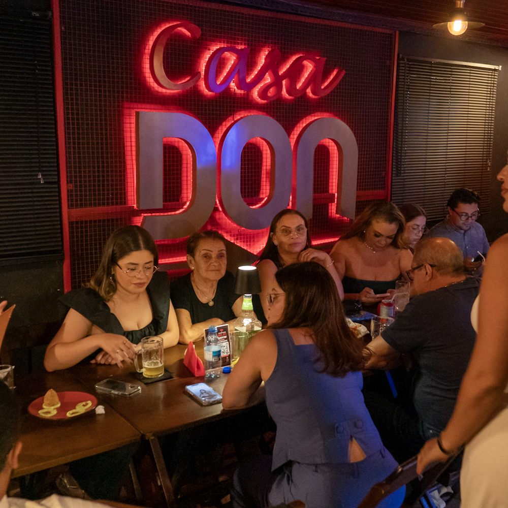 Salão cheio com o letreiro Casa Don aceso na parede