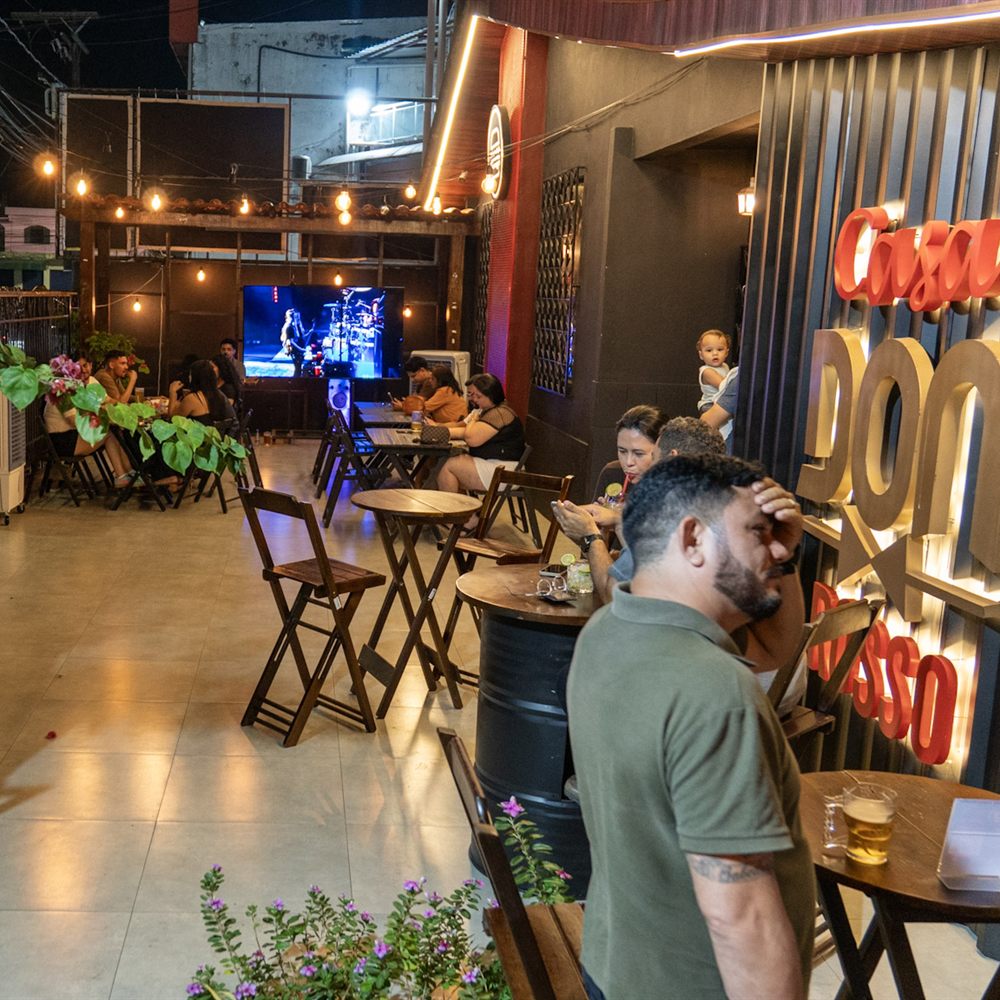 Salão da casa à noite, com o letreiro Casa Don e as mesas ao fundo